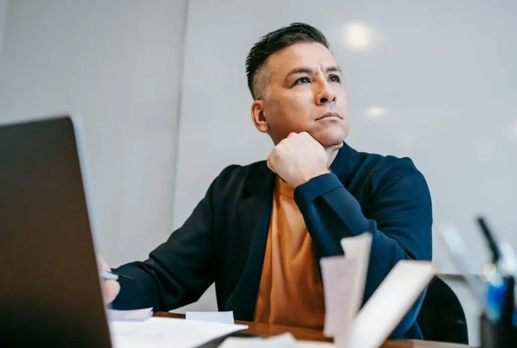 A focused man working remotely at a home office with a laptop and documents around.
